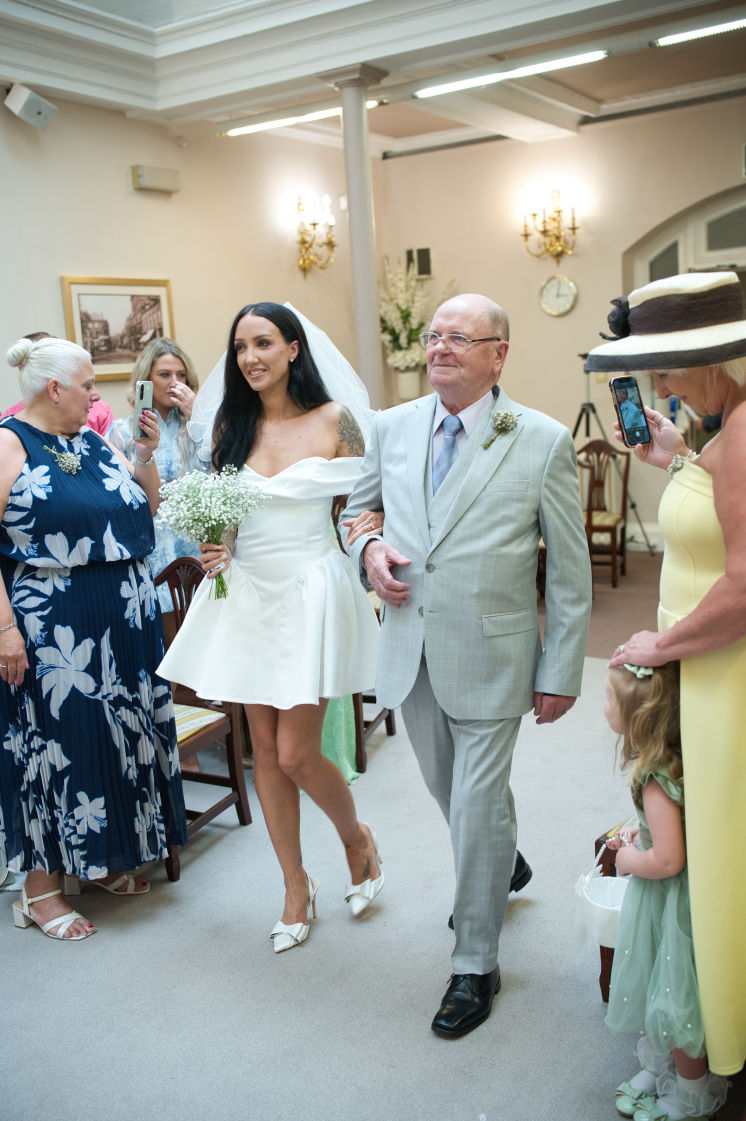 A bride been walked down the aisle by her grandfather at the, Sir A, Brumwelll Thomas room at Stockport registry office. at stockport town hall