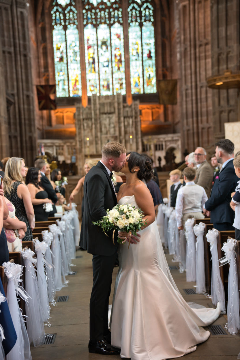 A bride and groom kiss half way down the isle of St Georges church Stockport 