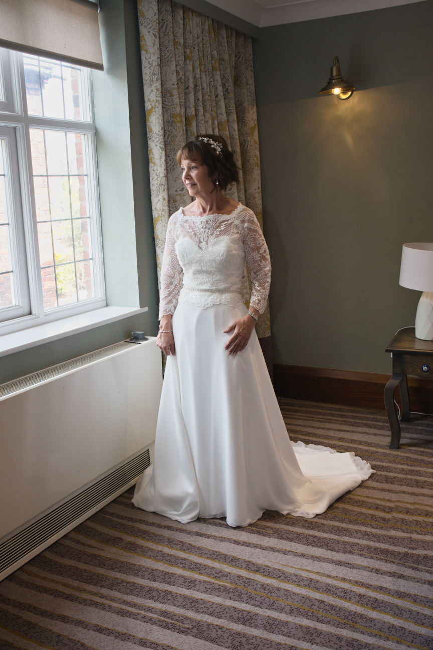 A bride  is looking out the window of her wedding room just before going down to the wedding ceremony at Stanneylands Wilmslow